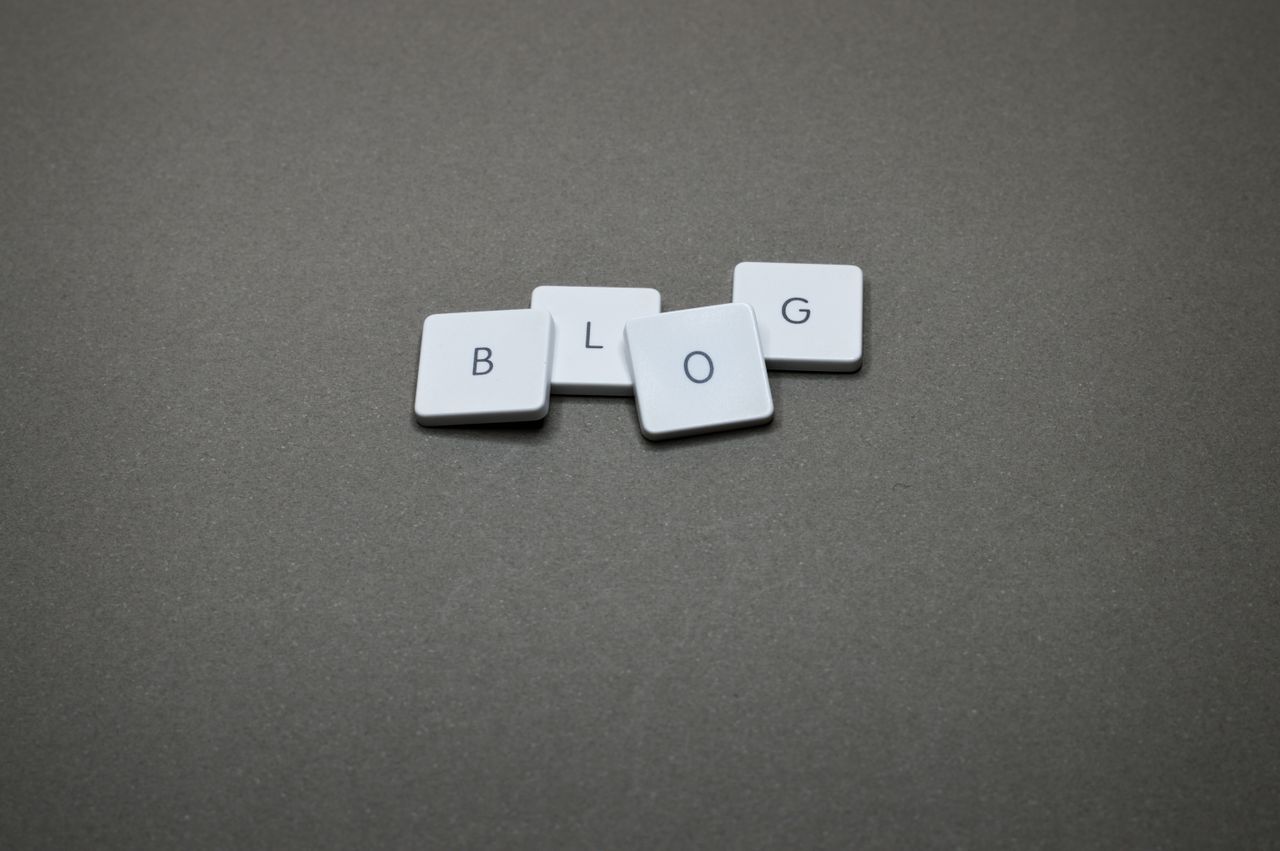 White Scrabble tiles spelling Blog against a minimalist gray background.